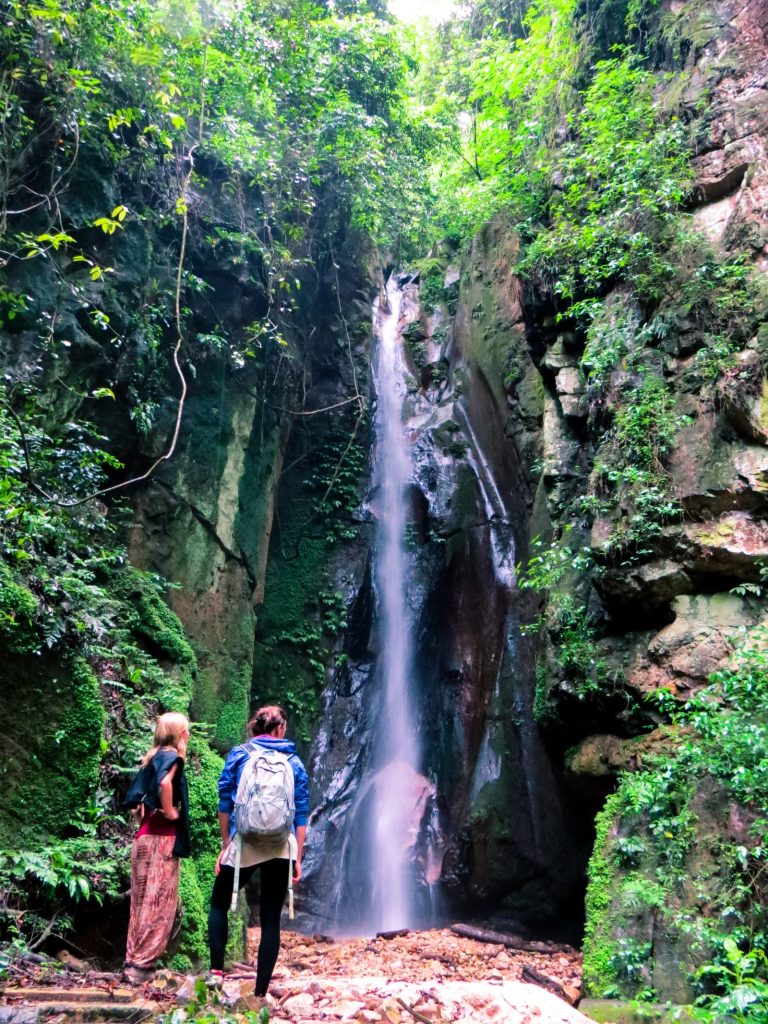 Two visitors looking up at Kakombe Waterfall in a forested gorge, Gombe National Park, Tanzania