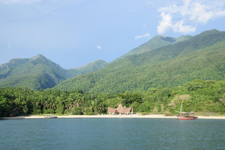 Forested peaks above beach camp with red hulled dhow moored, Mahale Mountains National Park, Tanzania