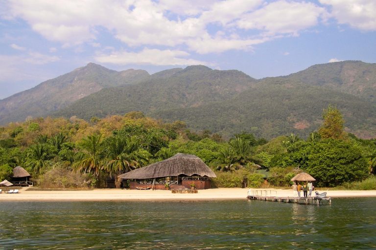 Four people on wooden jetty below beach lodge blue sky, Mahale Mountains National Park, Tanzania
