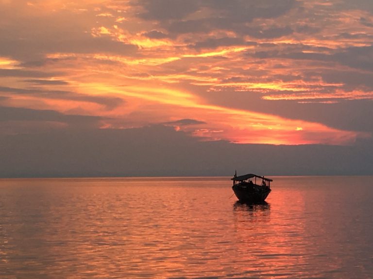 Lone canopied boat under fiery pink sunset sky, Mahale Mountains National Park, Tanzania