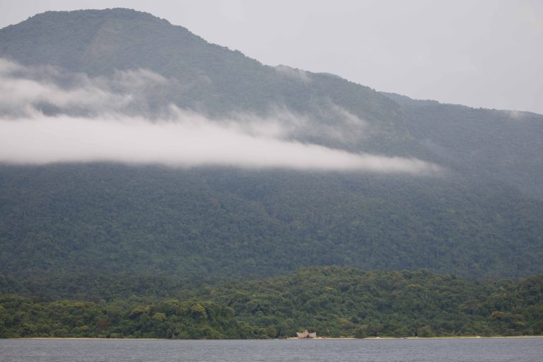 Low cloud band across forested slope above tiny shoreline lodge, Mahale Mountains National Park, Tanzania