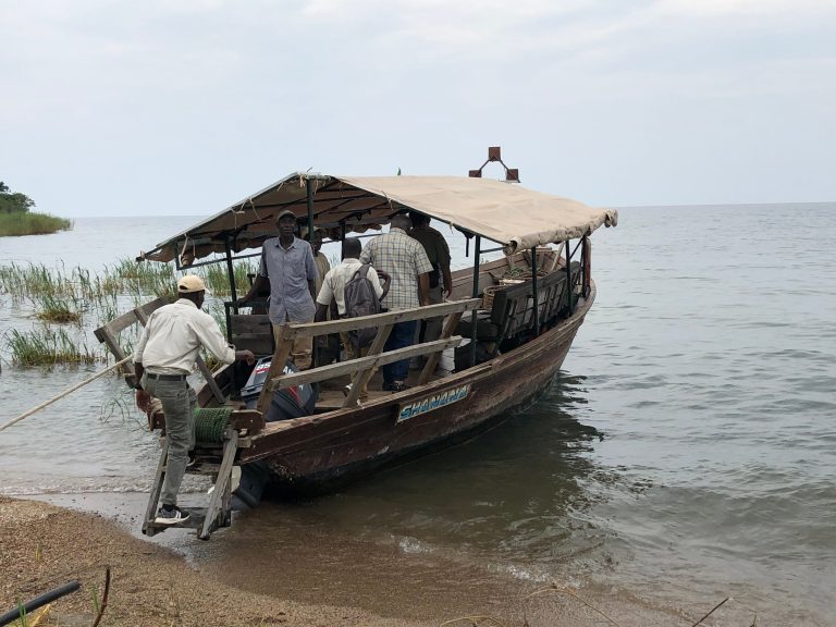 Men boarding canvas roofed wooden boat beached on shore, Mahale Mountains National Park, Tanzania