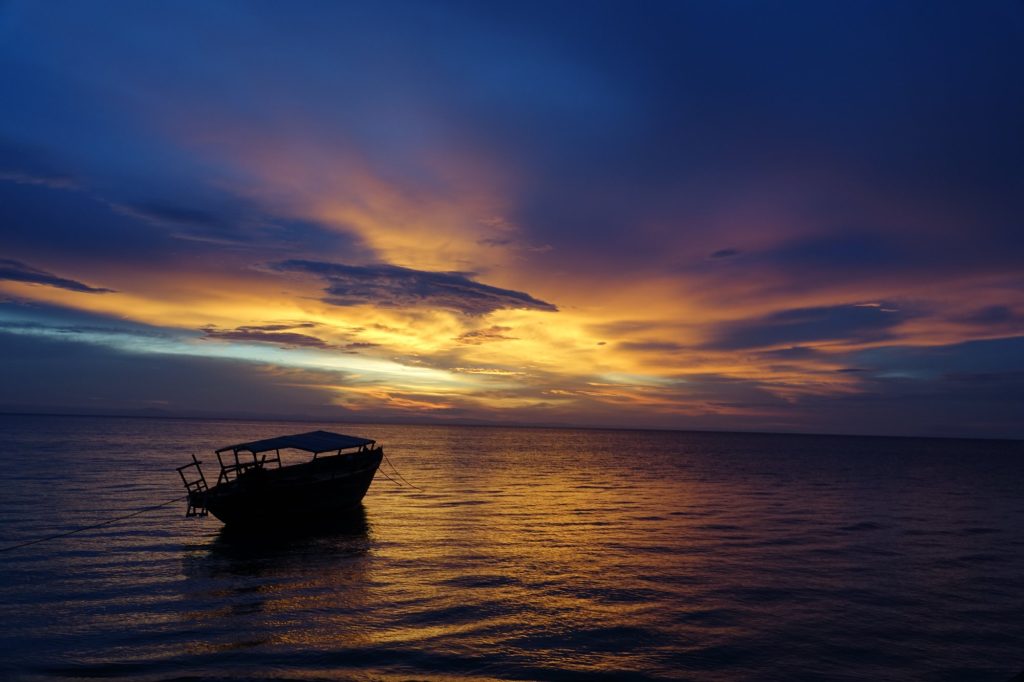Moored boat silhouetted against orange and blue sunset, Mahale Mountains National Park, Tanzania