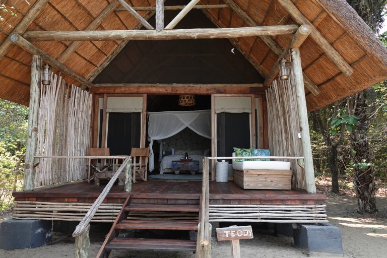 Open fronted stilted banda with mosquito net bed and name sign, Mahale Mountains National Park, Tanzania