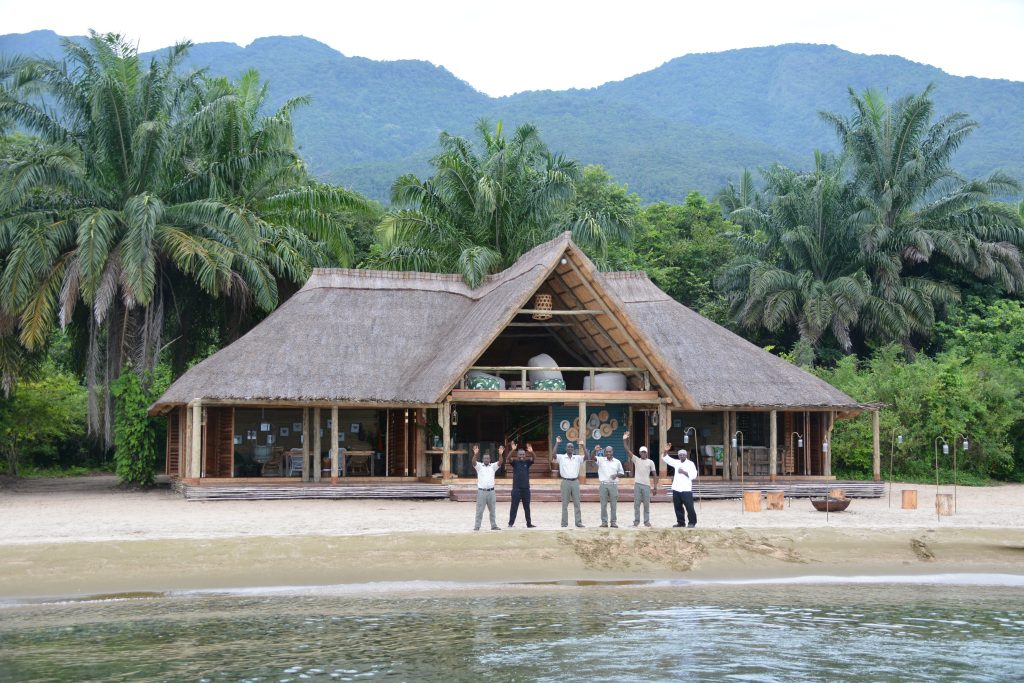 Six staff waving outside lakeside dining banda, Mahale Mountains National Park, Tanzania