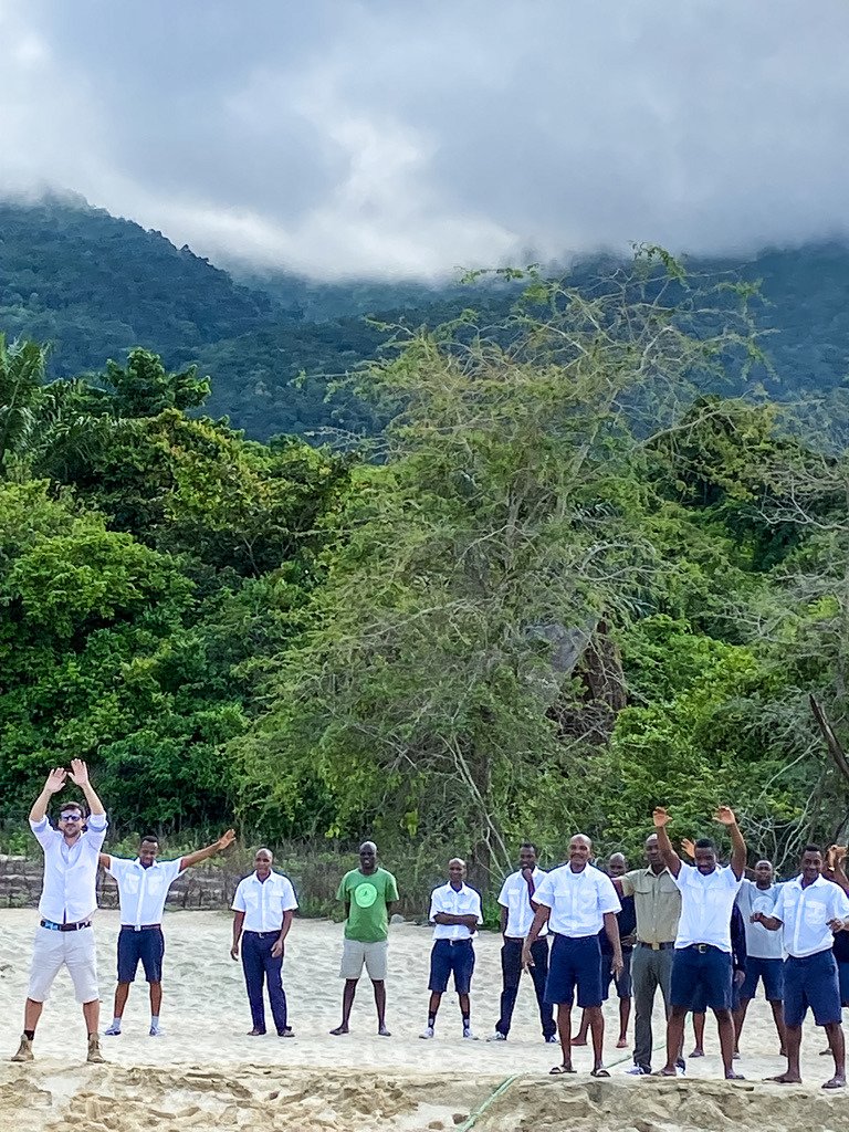 Camp guides and staff waving a welcome on the Lake Tanganyika beach at Mahale