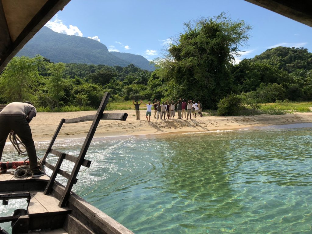 Staff waving farewell from beach seen from departing boat, Mahale Mountains National Park, Tanzania