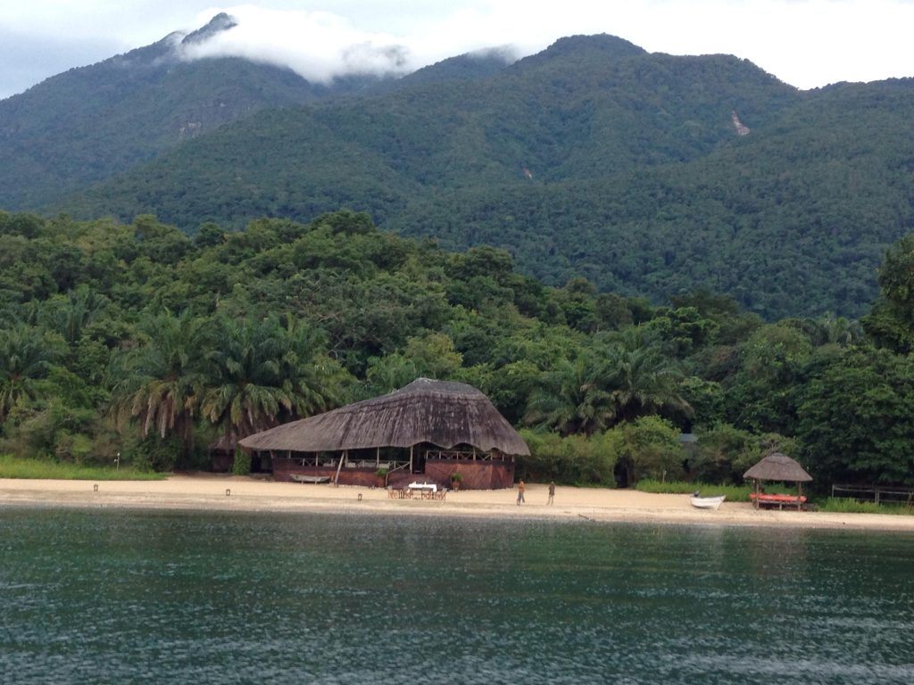 Thatched dining banda below cloud covered peak from lake, Mahale Mountains National Park, Tanzania