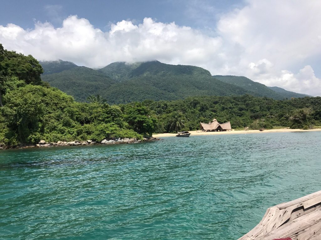 Turquoise bay and peaked thatch banda seen over boat bow, Mahale Mountains National Park, Tanzania