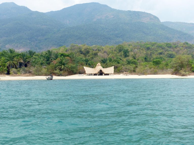 Turquoise lake and lone boat below hazy forested mountains, Mahale Mountains National Park, Tanzania
