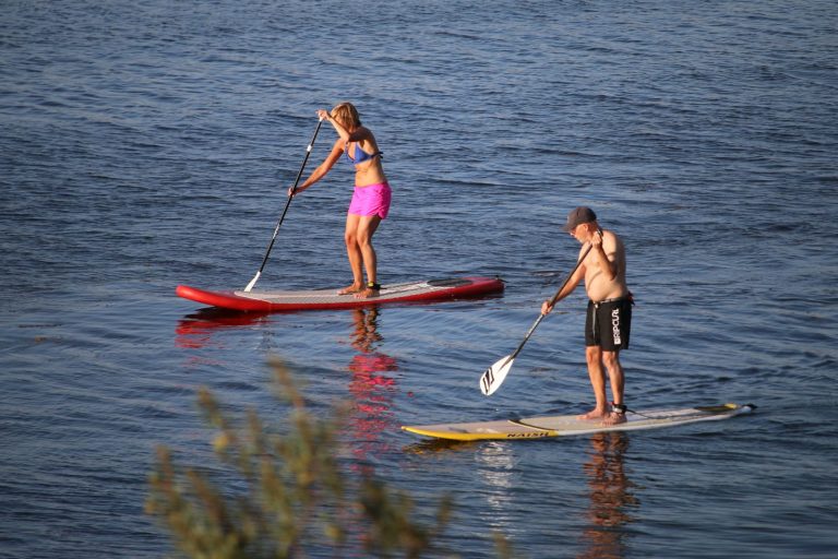 Two people stand-up paddleboarding on calm open lake water in evening light
